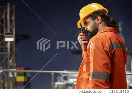 Offshore platform technician providing operational updates over walkie talkie network. Drilling rig employee maintaining radio contact with colleagues, monitoring machinery at night 135818410