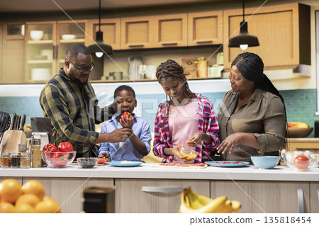 African american parents teaching kids how to make homemade pizza, explaining steps and ingredients list and cooking together. Black family bonding during culinary education activity. African american parents teaching kids how to make homemade pizza, explaining steps and ingredients list and cooking together. Black family bonding during culinary education activity. 135818454