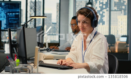 Developer listening music while working in AI startup training predictive models for language processing tasks. Tech expert wearing audio headphones uses technical expertise for IT tasks, camera B 135818506