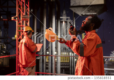 African american engineer exchanges insights on walkie talkie from drilling platform, coordinating fuel and natural petroleum extraction on offshore oil rig. Efficient fossil fuels production. African american engineer exchanges insights on walkie talkie from drilling platform, coordinating fuel and natural petroleum extraction on offshore oil rig. Efficient fossil fuels production. 135818551