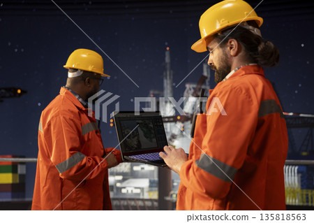 Drilling ship crew uses laptop to study geological maps for fossil fuel deposits. Offshore platform teamworking colleagues perform site assessment with digital mapping tech on notebook 135818563