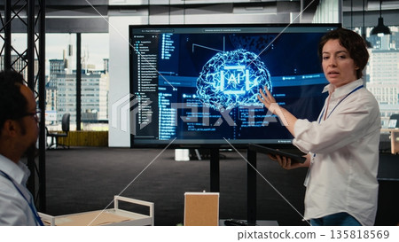 Investors gathered in tech startup boardroom to do deep dive into artificial intelligence. Programmer showcasing latest innovations in AI sector at corporate event in front of businesspeople, camera A Investors gathered in tech startup boardroom to do deep dive into artificial intelligence. Programmer showcasing latest innovations in AI sector at corporate event in front of businesspeople, camera A 135818569