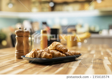 Empty kitchen table with croissants and homemade food for breakfast, contemporary apartment. Bright space with stylish kitchenware, fresh fruits and condiments on the counter, cozy home. Empty kitchen table with croissants and homemade food for breakfast, contemporary apartment. Bright space with stylish kitchenware, fresh fruits and condiments on the counter, cozy home. 135818574