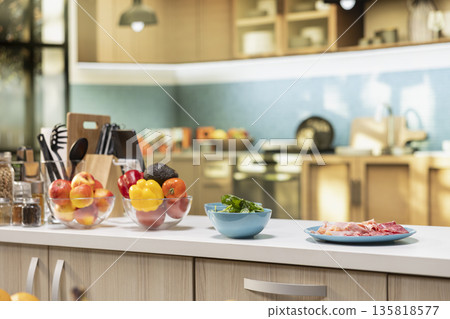 Empty cozy kitchen with a pizza prep area ready for cooking on the isle. Fresh ingredients like salami and herbs sitting on on the counter beside containers and utensils for homemade meal. 135818577