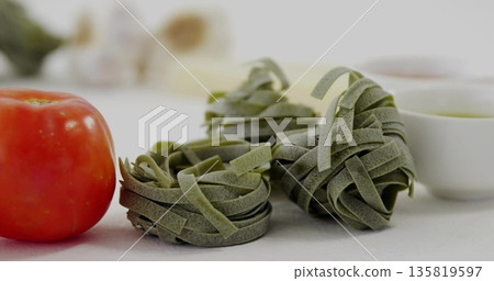 Showing three spinach pasta nests resting on kitchen countertop, with red tomato, garlic and bowls 135819597