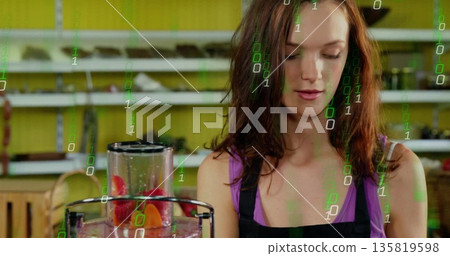 Juice attendant in purple top and apron blending fruit in juicer behind counter, green code overlay 135819598