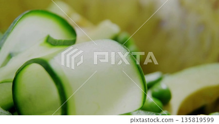 Curling thin cucumber ribbons resting on smooth plate surface, with green peas and squash pieces Curling thin cucumber ribbons resting on smooth plate surface, with green peas and squash pieces 135819599