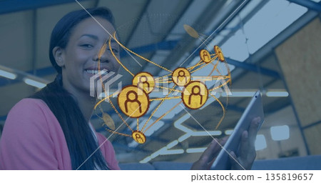 Smiling woman wearing cardigan holding tablet displaying golden network graphic in coworking space 135819657