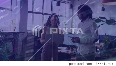 Discussing project details with coworkers while using laptop and smartphone in open-plan office 135819803