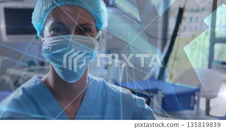 Standing nurse wearing blue scrub, respirator and hair cap in ward displaying graphics, equipment Standing nurse wearing blue scrub, respirator and hair cap in ward displaying graphics, equipment 135819839