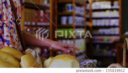 Reaching shopper wearing sleeveless top grabbing bread in wicker basket at bakery table, copy space Reaching shopper wearing sleeveless top grabbing bread in wicker basket at bakery table, copy space 135819912