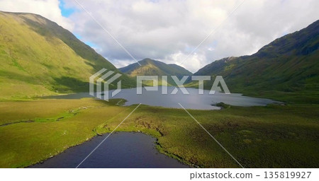 Showcasing central lake reflecting cloud formations in mountain valley, with pond and grassy meadow Showcasing central lake reflecting cloud formations in mountain valley, with pond and grassy meadow 135819927