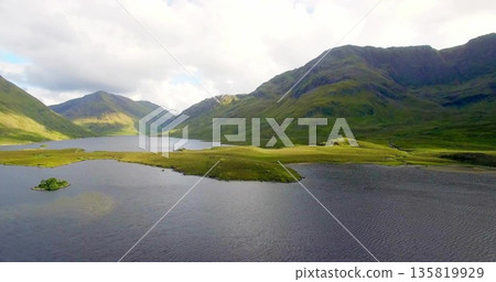Showcasing grassy peninsula stretching into highland lake basin, with small islet and sunlit slopes 135819929