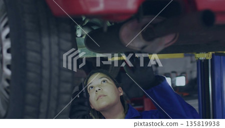 Mechanic wearing coveralls black gloves checking exhaust under lifted red car at garage Mechanic wearing coveralls black gloves checking exhaust under lifted red car at garage 135819938