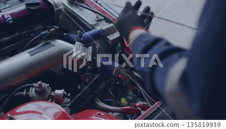 Mechanic wearing coveralls and glove inspecting aluminum intake pipe in garage, with silicone hoses Mechanic wearing coveralls and glove inspecting aluminum intake pipe in garage, with silicone hoses 135819939