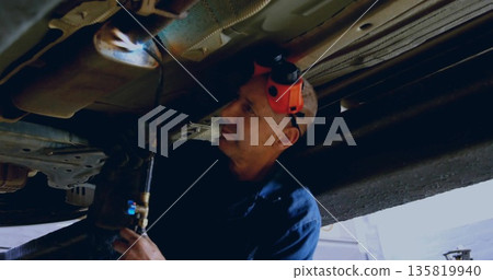 Mechanic wearing coveralls and earmuffs cutting undercarriage with torch in workshop, copy space Mechanic wearing coveralls and earmuffs cutting undercarriage with torch in workshop, copy space 135819940