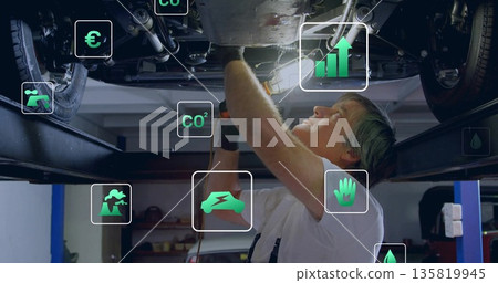Drilling mechanic using power drill under vehicle chassis on lift in workshop, with overlay icons 135819945