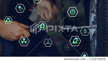 Mechanic in coveralls applying torque on car wheel in workshop, with lug wrench and eco symbols 135819948