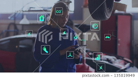Holding tablet woman mechanic in coverall inspecting car in workshop with car lift, emission icons 135819949