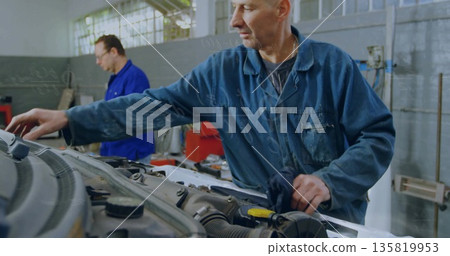 Wiping front mechanic reaching across engine bay in vehicle repair workshop, with open car hood Wiping front mechanic reaching across engine bay in vehicle repair workshop, with open car hood 135819953
