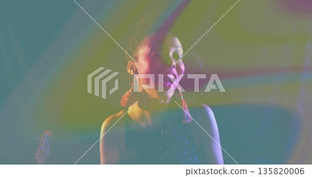 Singing performer wearing sequin top onstage, with colored lights, smoke haze and guitar headstock 135820006