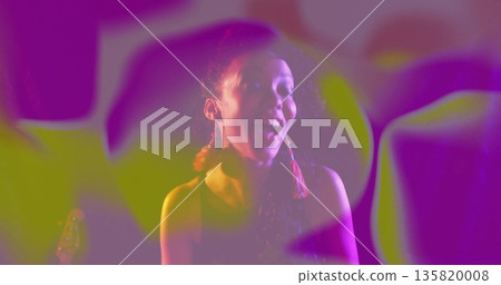 Woman with red tassel earrings and top laughing in studio, with light projections, guitar headstock Woman with red tassel earrings and top laughing in studio, with light projections, guitar headstock 135820008