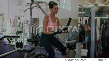 Exercising woman in pink sportswear on elliptical trainer in gym, highlighting financial charts Exercising woman in pink sportswear on elliptical trainer in gym, highlighting financial charts 135820014