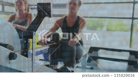 Pulling workout duo wearing tank tops and leggings rowing on rowing machines in gym, step platforms Pulling workout duo wearing tank tops and leggings rowing on rowing machines in gym, step platforms 135820016