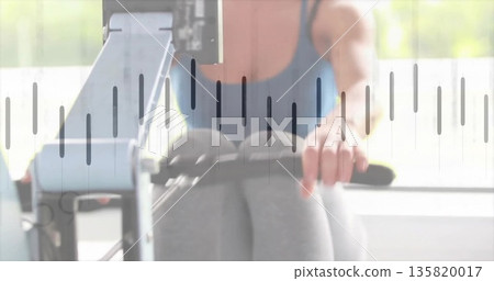 Rowing exerciser gripping rower handle near window in gym, wearing blue tank top, gray leggings Rowing exerciser gripping rower handle near window in gym, wearing blue tank top, gray leggings 135820017