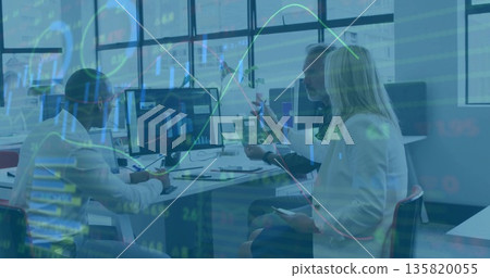 Three coworkers reviewing computer monitor charts in office, with tablet, smartphone and report 135820055