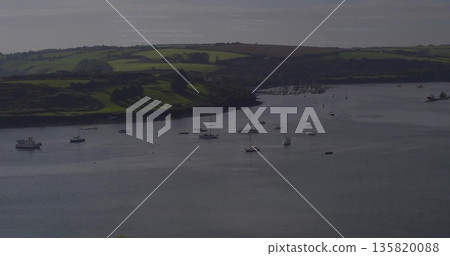 Floating anchored sailboats and small yachts drifting across calm estuary bay, with mooring buoys 135820088