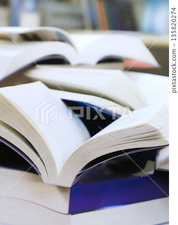 stack of books, close up. Open book on the table in library. Back to school concept. Open book on table with blur bookshelf background stack of books, close up. Open book on the table in library. Back to school concept. Open book on table with blur bookshelf background 135820274