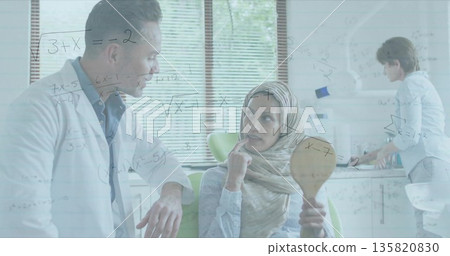 Leaning male doctor speaking with seated patient in bright clinic room, with handheld mirror 135820830