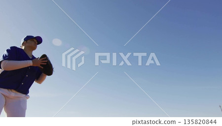 Teenage girl wearing blue jersey, cap raising black glove on field under clear sky, copy space Teenage girl wearing blue jersey, cap raising black glove on field under clear sky, copy space 135820844