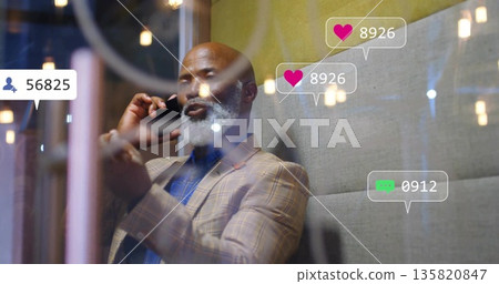 Talking businessman in suit holding smartphone in lounge, with pendant lights and social icons Talking businessman in suit holding smartphone in lounge, with pendant lights and social icons 135820847