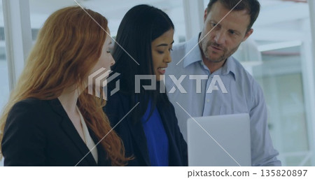 Collaborating business professionals analyzing report on laptop in modern office glass partitions 135820897