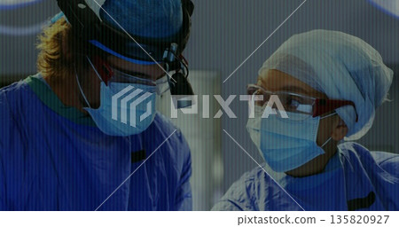 Operating surgeons wearing scrubs and masks doing surgery in operating room with headlight loupes 135820927