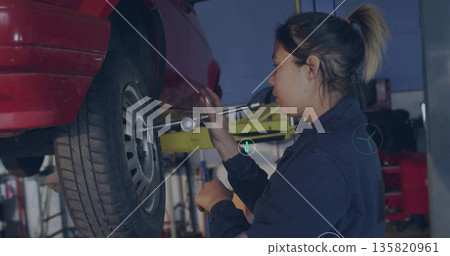 Using torque wrench, mechanic in coveralls tightening lugnut on car wheel in repair bay, copy space 135820961