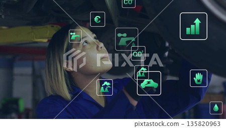 Inspecting mechanic in blue coverall and gloves under vehicle in garage with floating data icons Inspecting mechanic in blue coverall and gloves under vehicle in garage with floating data icons 135820963