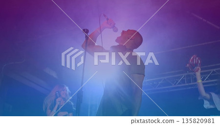 Gripping microphone singer belting out song on stage, with red maracas and colored LED lights 135820981