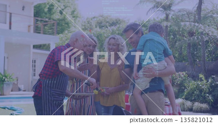 Multigenerational family in summer clothes grilling food on backyard lawn, with grill and spatula 135821012