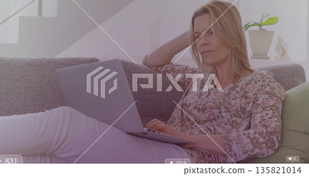 Typing woman wearing floral blouse working on laptop on sofa in living room, with plant, figurine Typing woman wearing floral blouse working on laptop on sofa in living room, with plant, figurine 135821014