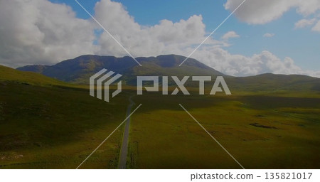 Cutting narrow single-lane paved road slicing through grassy plains toward distant mountain peaks Cutting narrow single-lane paved road slicing through grassy plains toward distant mountain peaks 135821017