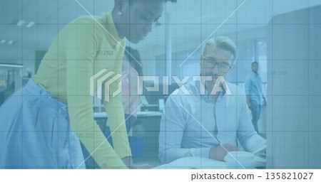 Collaborating woman, man wearing business attire leaning over desk at corporate office, with laptop 135821027