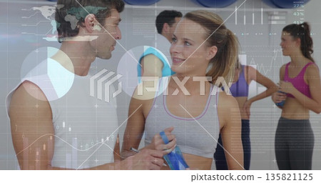 Two participants in sportswear talking in fitness studio with blue water bottles, exercise balls 135821125
