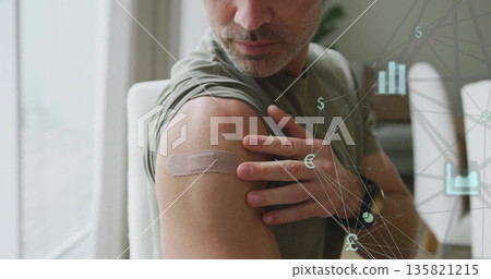Mature man pulling up sleeve, showing adhesive bandage in home dining area, with digital overlay 135821215