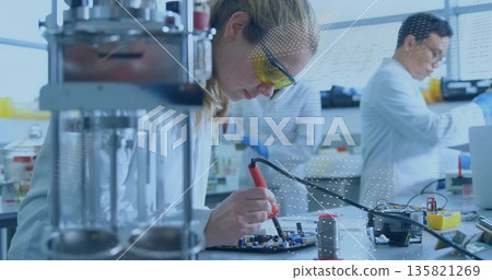 Female engineer in lab coat soldering circuit board in electronics lab, with soldering iron Female engineer in lab coat soldering circuit board in electronics lab, with soldering iron 135821269