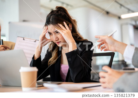 Asian businesswoman holding head getting stress or exhausted over workplace dispute at office table Asian businesswoman holding head getting stress or exhausted over workplace dispute at office table 135821379