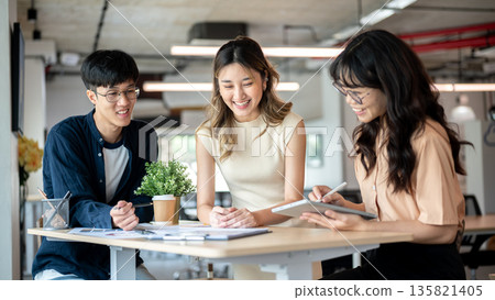 Pretty asian woman designer smiling or laughing with coworkers at wooden table in the office. 135821405