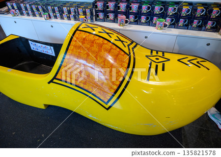 Large yellow wooden clog display with traditional Dutch design, surrounded by colorful mugs on a shelf. Large yellow wooden clog display with traditional Dutch design, surrounded by colorful mugs on a shelf. 135821578